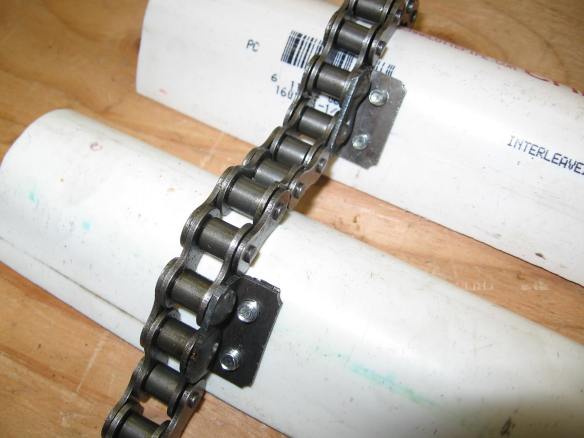Black #40 steel roller chain holding white PVC scoops.  The far side of the scoops dig and lift the moon dust.